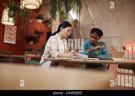 Porträt zweier ethnischer Studenten, die gemeinsam an einem Projekt arbeiten, während sie an einem Tisch im Café studieren, Kopierraum Stockfoto