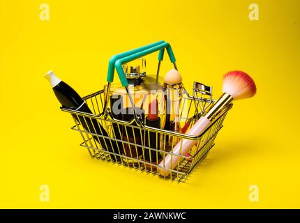Makeup Produkte Fondant, Mascara, Parfüm, Pinsel, mit Kosmetikbeutel Warenkorb auf Farbe Hintergrund gelb Stockfoto