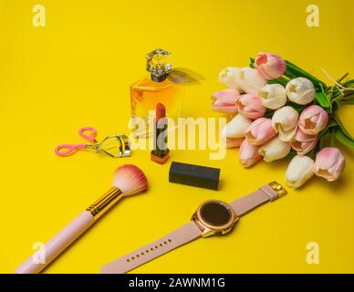 Makeup Produkte Fondant, Mascara, Parfüm, Pinsel, Blumen mit Kosmetikbeutel Warenkorb auf gelbem Hintergrund Stockfoto