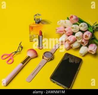 Makeup Produkte Fondant, Mascara, Parfüm, Pinsel, Blumen Uhr, Handy mit Kosmetiktasche auf gelbem Hintergrund Stockfoto