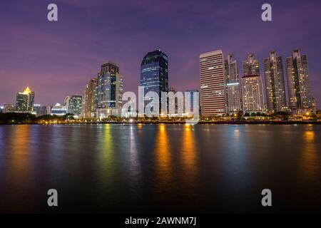 Blick auf die modernen Wolkenkratzer hinter einem See im Benjamin (Benjamin akitti) Park in der Innenstadt von Bangkok, Thailand, in der Abenddämmerung. Stockfoto