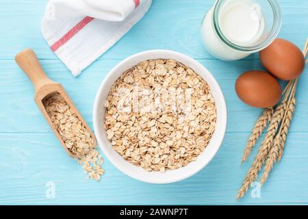 Haferflocken oder gerollte Hafer in Schüssel, Flasche Milch und Hühnereiern. Blauer Holztisch. Tabelle Draufsicht auf gesunde Frühstücksgerichte Stockfoto