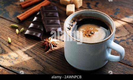 Kaffee und Gewürze Sternanis, Zimtstangen, Kardamompoden und dunkle Schokoladenrinde auf Holztisch. Frühstückskonzept Stockfoto