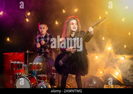 Kinder geben vor, in einer Rockband zu sein und im Studio oder auf der Bühne zu spielen und zu singen. Mädchen spielen an Gitarre und Junge am Schlagzeug. Stockfoto