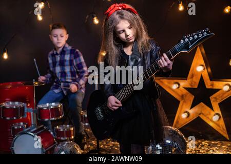 Kinder geben vor, in einer Rockband zu sein und im Studio oder auf der Bühne zu spielen und zu singen. Mädchen spielen an Gitarre und Junge am Schlagzeug. Stockfoto