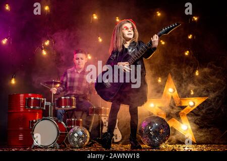 Kinder geben vor, in einer Rockband zu sein und im Studio oder auf der Bühne zu spielen und zu singen. Mädchen spielen an Gitarre und Junge am Schlagzeug. Stockfoto