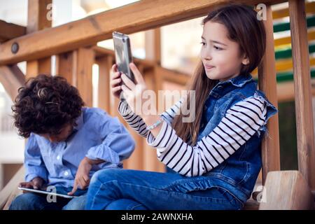 Zwei Kinder Jungen und Mädchen spielen Spiele auf Tablet im Freien. Kinder- und Gadget-Suchtkonzept Stockfoto