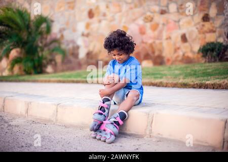 Ein kleiner Junge auf Rollerskaten fiel herab und spürt Schmerzen. Kinder-, Leier- und Gesundheitskonzept Stockfoto