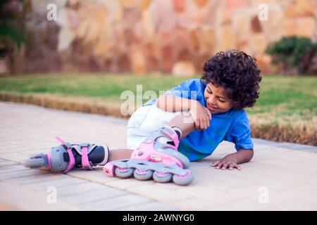 Ein kleiner Junge auf Rollerskaten fiel herab und spürt Schmerzen. Kinder-, Leier- und Gesundheitskonzept Stockfoto