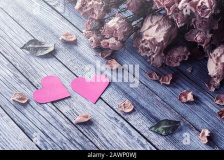 Zwei Papierherzen und trockene Rosen auf Holztisch, Erinnerungen an vergangene Liebe, valentinstag Stillleben Stockfoto