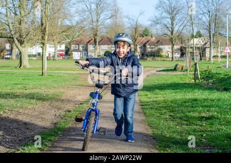 Porträt eines glücklichen jungen Jungen mit seinem Fahrrad, der im Park einen Fahrradhelm trägt. Stockfoto