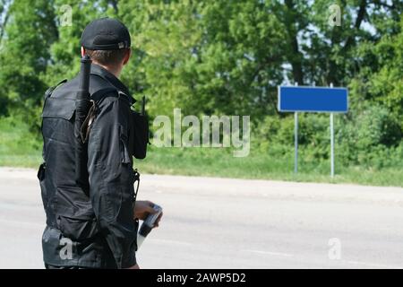 Der Beamte inspiziert die Straße. Der Offizier steht mit dem Rücken in schwarzer Uniform Stockfoto
