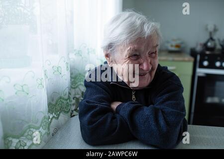 Eine alte Rentnerin lacht sitzend am Tisch. Stockfoto