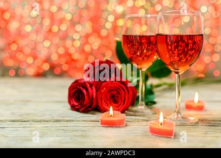 Valentinstag Konzept. Zwei Gläser Wein, rote Rosen und brennende Kerzen auf einem alten Holztisch vor einem verschwommenen leuchtenden Hintergrund mit Kopie Stockfoto