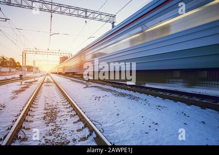 Hochgeschwindigkeitszug fährt schnell durch den Bahnhof zur Winteruntergangszeit. Stockfoto