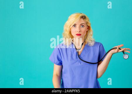 Nahaufnahme des Studioporträts einer jungen Ärztin oder Krankenschwester, die blaue Schrubben mit der Hand und dem Ausdruck überraschter Ungläubigkeit trägt Stockfoto