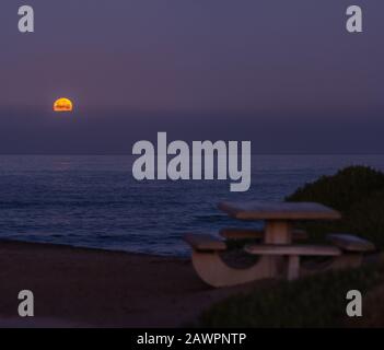 Der Vollmond im Februar setzt im Morgengrauen über den Pazifischen Ozean, wie er vom kalifornischen Strand aus gesehen wird. Stockfoto