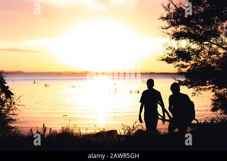 Silhouette zweier Jungs und der Sonnenuntergang über dem Guaiba See in Porto Alegre, Brasilien Stockfoto