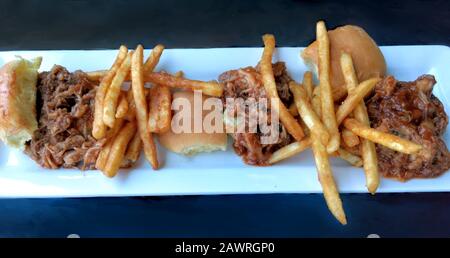 Drei Schweineschieber haben zartes, würzig gezogenes Schweinefleisch in einer Grillsauce und knusprige pommes frites Stockfoto