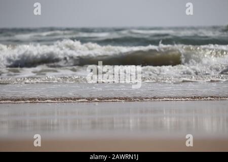 Brillanter Schuss von großer Meereswasserwelle am Strand gegen blauen Himmel mit Sandvordergrund, Strandlandschaft Stockfoto