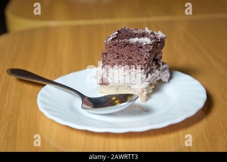 Weißer, gehackter Background aus Kuchenteig in einem weißen Teller. Löffel. Brauner und weißer Kuchen auf Holzbrett . Kuchen mit Keks und Sahne. Aus Holz Stockfoto
