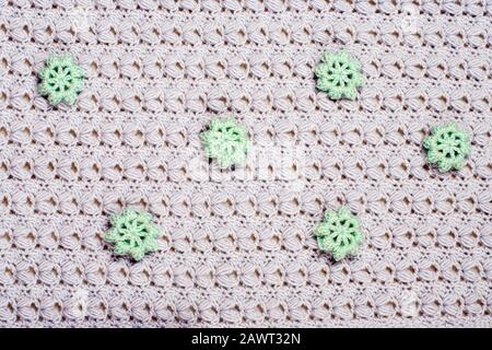 Schöne graue Strickstruktur. Elegantes Muster mit aufwändig gebundenen und genähten grünen Blumen. Häkelnaht. Hintergrund für Design. Stockfoto