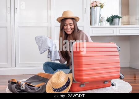 Reisender junger asiaten bereiten Stoff und Sachen in orangefarbenen Koffer für den Urlaub zu Hause vor.Backpacker Reisekonzept Stockfoto