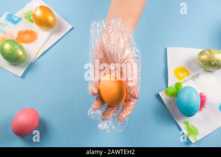 Eine weibliche Hand in einem Handschuh hält neben anderen bemalten Eiern auf blauem Grund nur ein bemaltes Osterei. Stockfoto