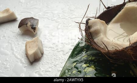 Gehackte Kokosnuss- und Kokosmasse auf einem weißen Holztisch. Kokosnuss und Kokosnussmilch auf einem leichten Tisch. Gesundes Esskonzept. Vegan, keine Milchprodukte. Stockfoto