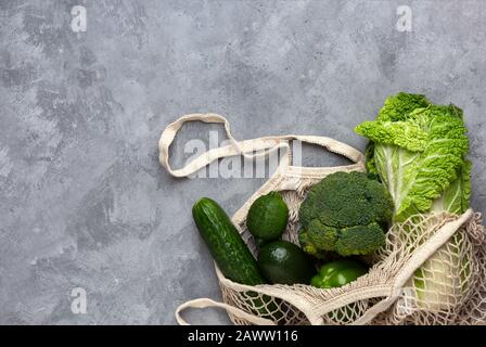 Grünes frisches Gemüse in einem Saitenbeutel auf grauem Betonhintergrund. Flaches Layout mit Kopierbereich. Stockfoto