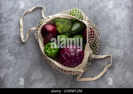 Grüne und violette Produkte in einer Eco-Tasche auf grauem Hintergrund. Null-Abfall-Konzept, Draufsicht Stockfoto