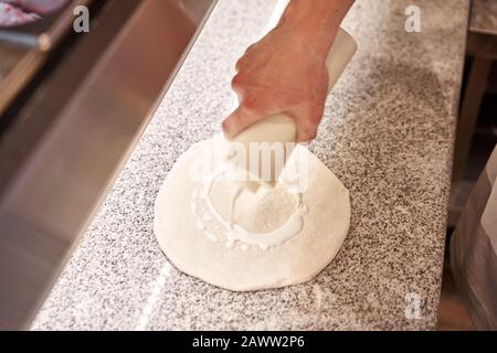 Pizza kochen. Legt Champignons und Sahnesauce aus, Zutaten auf der Teigvorform. Nahaufnahme der Küchenchef-Bäckerei in einer einheitlichen weißen Schürze in der Küche Stockfoto