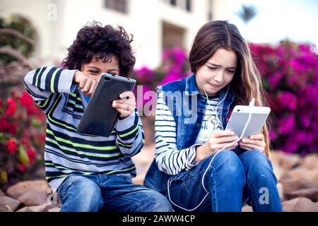 Zwei Kinder Jungen und Mädchen spielen Spiele auf Tablet im Freien. Kinder- und Gadget-Suchtkonzept Stockfoto