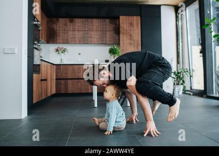 Vater steht auf den Fingern, während er den Kopf seines Babys küsst. Stockfoto