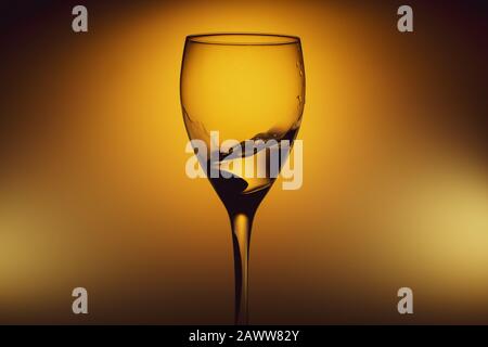 Wasser spritzt in Glas auf glühendem Hintergrund. Spritzendes Wasser im Weinglas. Transparenter Cocktail Stockfoto