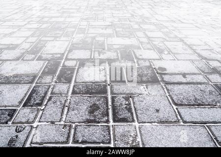 Steinerner Gehweg aus grauem Granit, schneebedeckt. Struktur des Straßenbelags Stockfoto