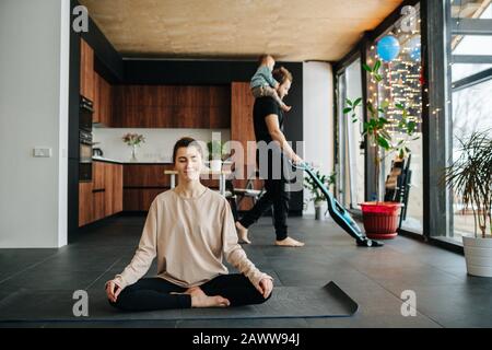 Frau sitzt in leichter Pose, während ihr Mann mit Baby am Hals auf dem Boden saugt Stockfoto