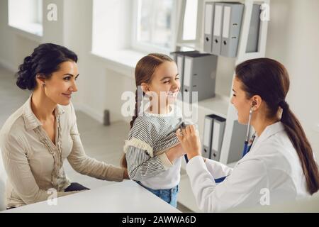 Eine Frau Kinderärztin macht eine Setoskop-Untersuchung an ein Kindermädchen mit Mutter in einem Klinikbüro. Stockfoto