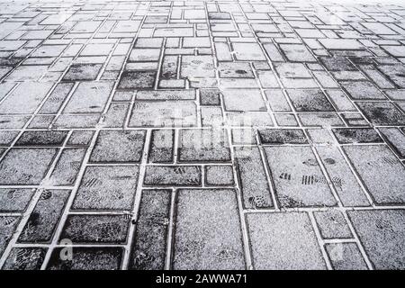 Steinerner Gehweg aus grauem Granit, schneebedeckt. Struktur des Straßenbelags Stockfoto