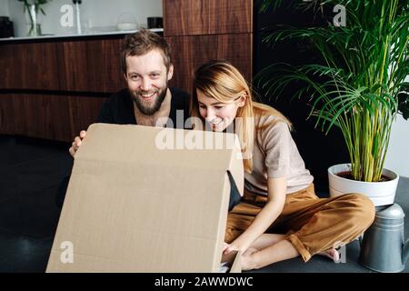Fröhliches modernes Paar, das auf einem Boden sitzt, der quer durchgestielt ist und sich öffnet. Stockfoto