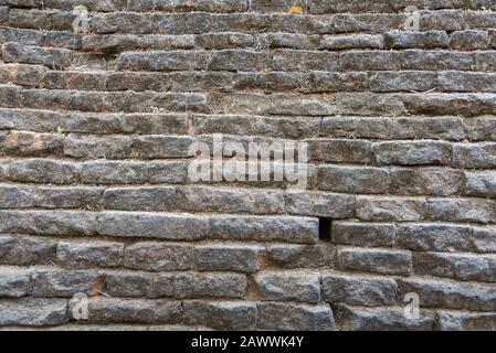 Die Mauer aus Granit besteht aus Schichten von Platten, die mit grobem Mörtel aus Ton befestigt sind. Gemusterte Textur. Stockfoto