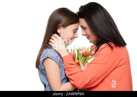 Fröhlicher Muttertag, Frauentag oder Geburtstagshintergrund. Adliges Mädchen, das Mutter Blumenstrauß mit rosafarbenen Tulpen schenkt. Studio-Porträt einer liebenden Mutter, die sich umarmt Stockfoto