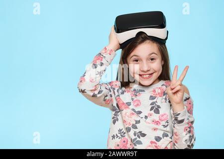 Studio-Porträt eines süßen jungen kaukasischen Mädchens, das eine virtuelle Reality-Brille vor pastellblauem Hintergrund trägt. Zukünftiges Technologiekonzept für Gadgets. Stockfoto