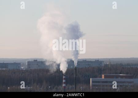 Rauchwolke steigt aus dem indastrischen Schornstein vor dem wolkenigen Himmel auf. Indastridalzone in der Stadt Russland. Winterliches Stadtbild mit Gebäuden und Park. Stockfoto mit leerem Textbereich. Stockfoto