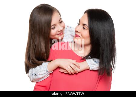 Taille up Studio Portrait von niedlichen und verspielten Schulmädchen, die ihre Mutter umarmten. Fröhliche Familie lächelnder Hintergrund isoliert über weiß. Stockfoto