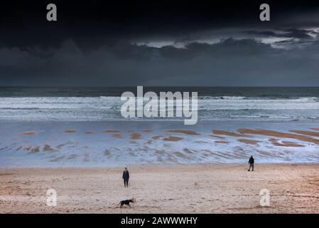 Hundegänger und ihre Haustiere am Fistral Beach, während dunkle Regenwolken Newquay in Cornwall nähern. Stockfoto