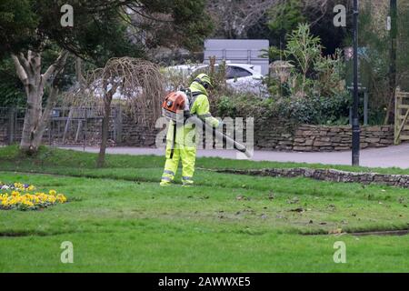 Ein Gartenpfleger, der Hi-Vis-Kleidung mit einem Stihl-Luftgebläse trägt, um abgestorbene Blätter in den Trenance Gardens in Newquay in Cornwall abzublasen. Stockfoto