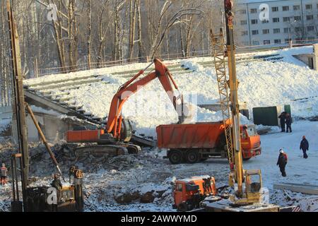 Bagger lädt im Winter in Russland Erde in einen LKW an einer Baustelle. Stockfoto