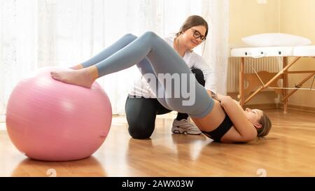 Physiotherapeuten arbeiten mit jungen weiblichen Client auf die Kernkompetenz mit fitball. Rehabilitation und Physiotherapie Hintergrund. Stockfoto