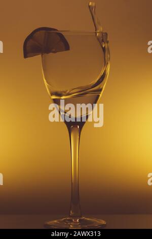 Wasser spritzt in Glas auf glühendem Hintergrund. Spritzendes Wasser im Weinglas. Transparenter Cocktail Stockfoto